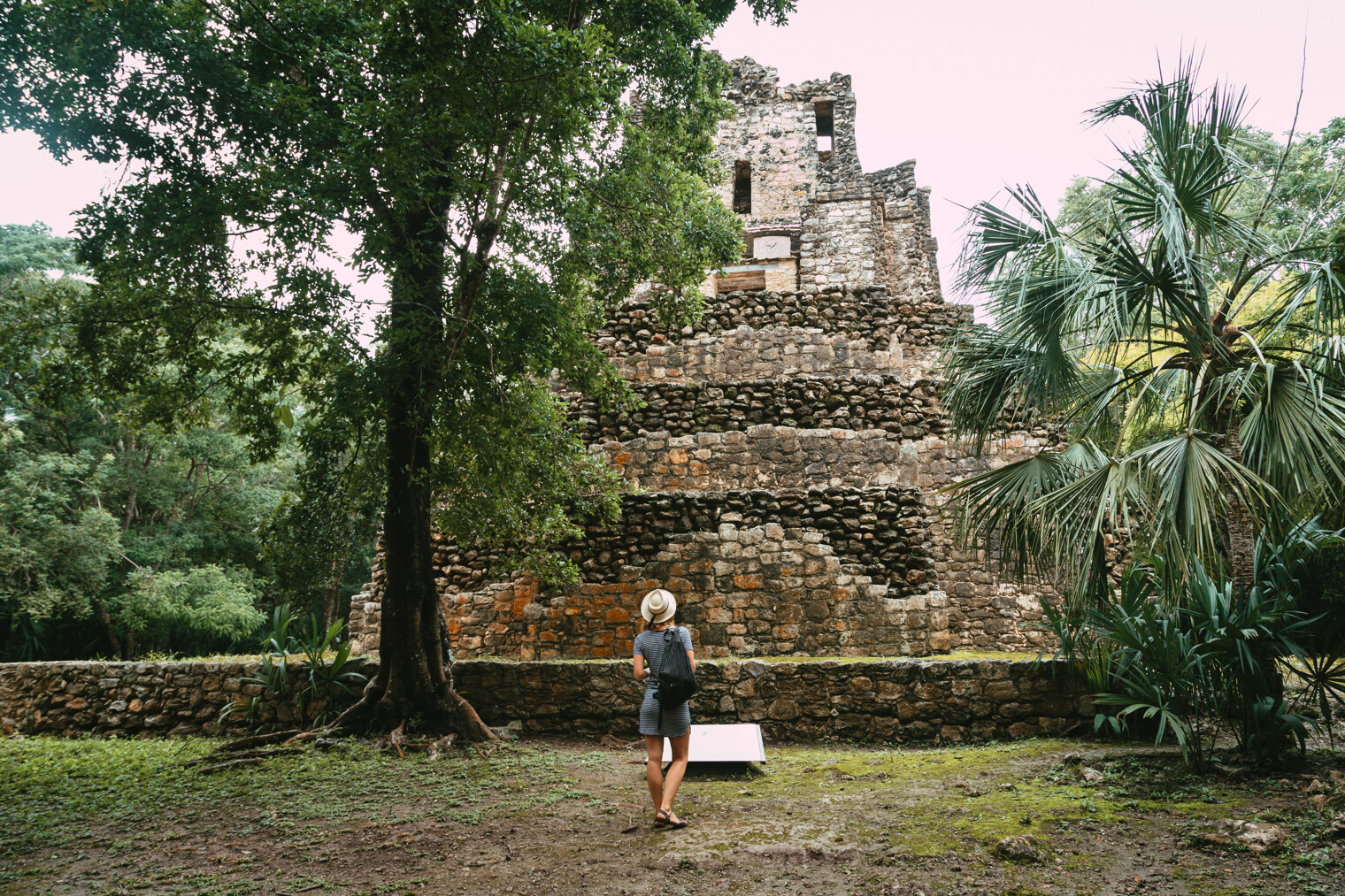 Une femme de dos face à un site archéologique Maya dans le Yucatan