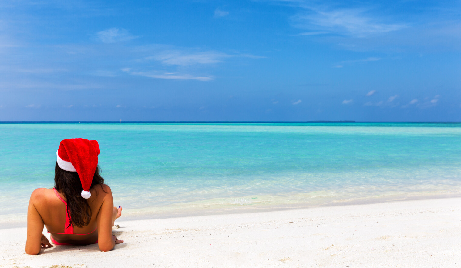 Une femme seule de dos allongée sur le sable blanc d'une plage paradisiaque