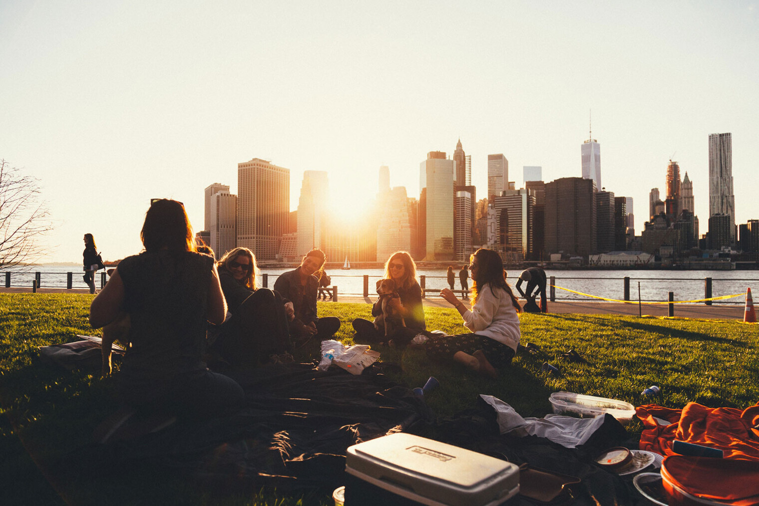 Un groupe de jeunes femmes en train de pic-niquer avec des building et le coucher de soleil en fond