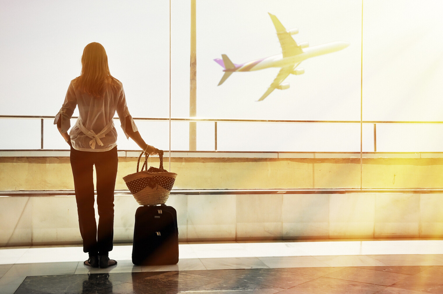 Une femme de dos à l'aéroport qui regarde un avion décoller