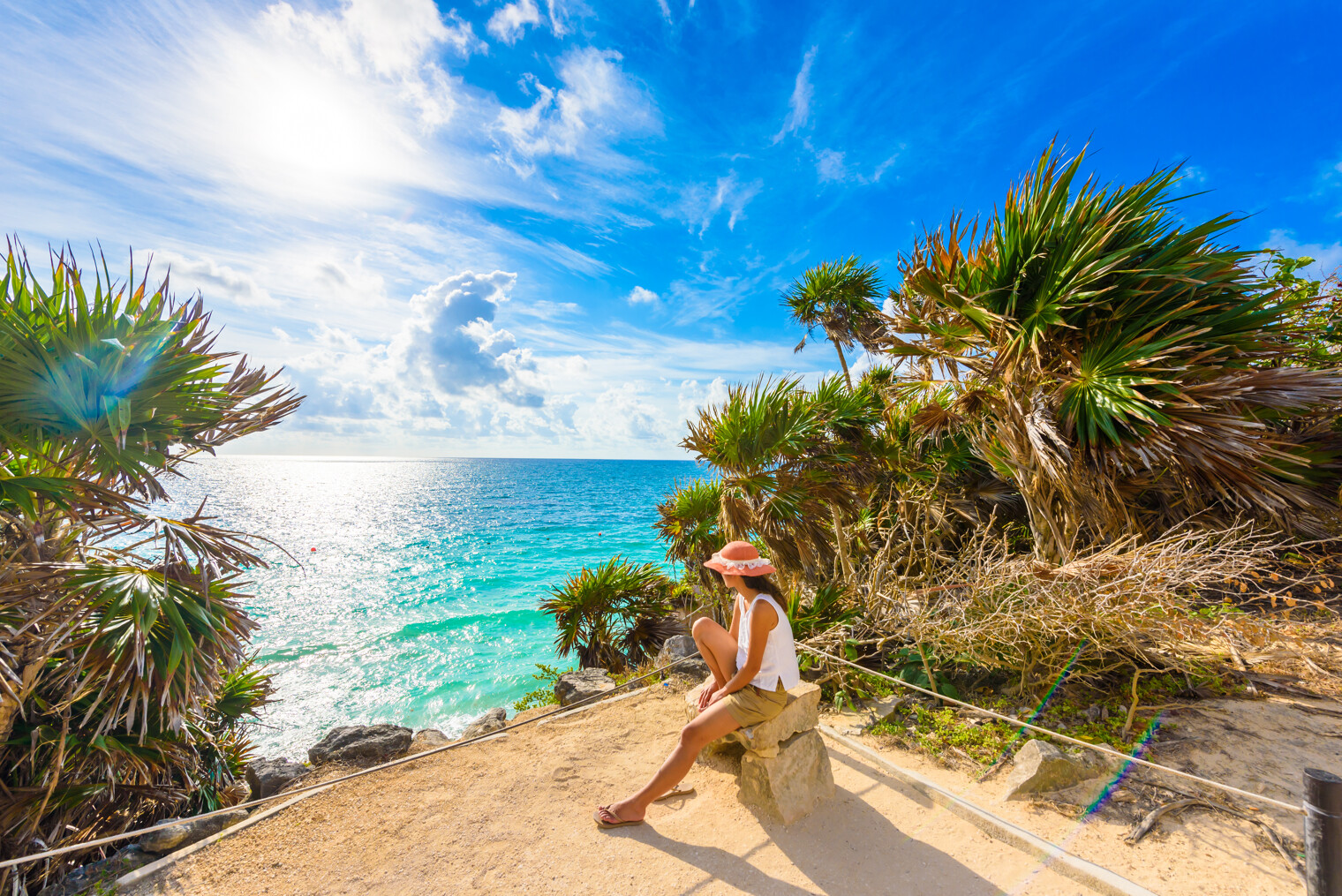 Une femme assise sur un rocher regardant la mer des Caraïbes à Tulum