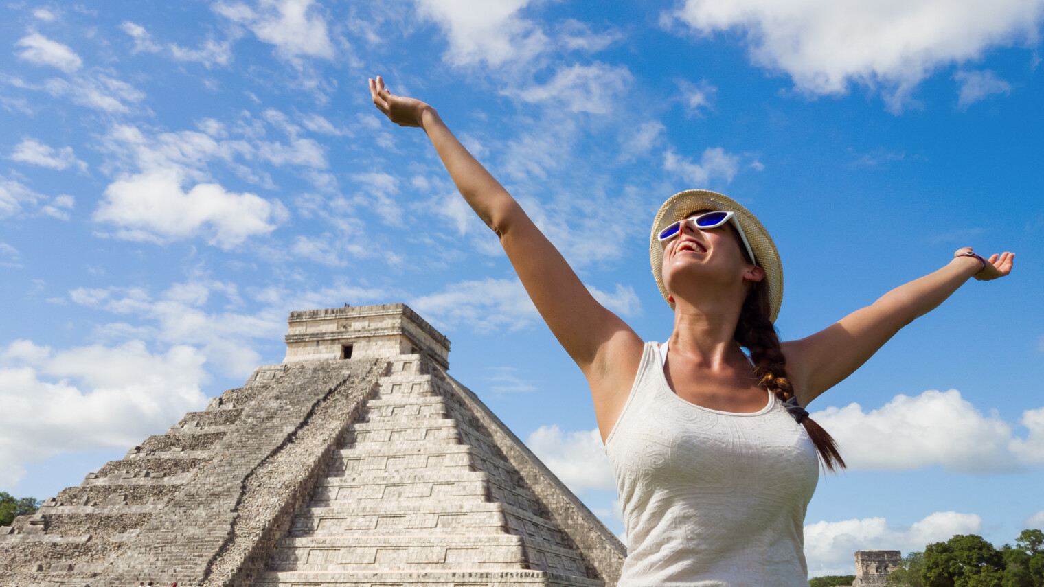 Une femme heureuse bras en l'air devant l'une des pyramide de Chichen Itza au Mexique