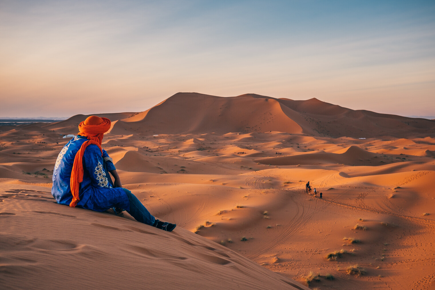 Un touareg assis sur une dune face au désert de Merzouga