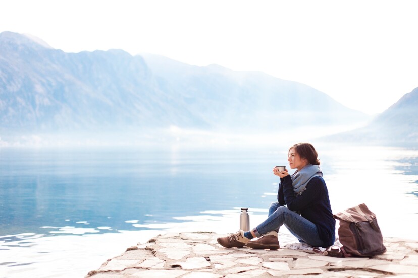 Une femme seule assise avec une tasse à café à la main au bord d'un lac de montagne