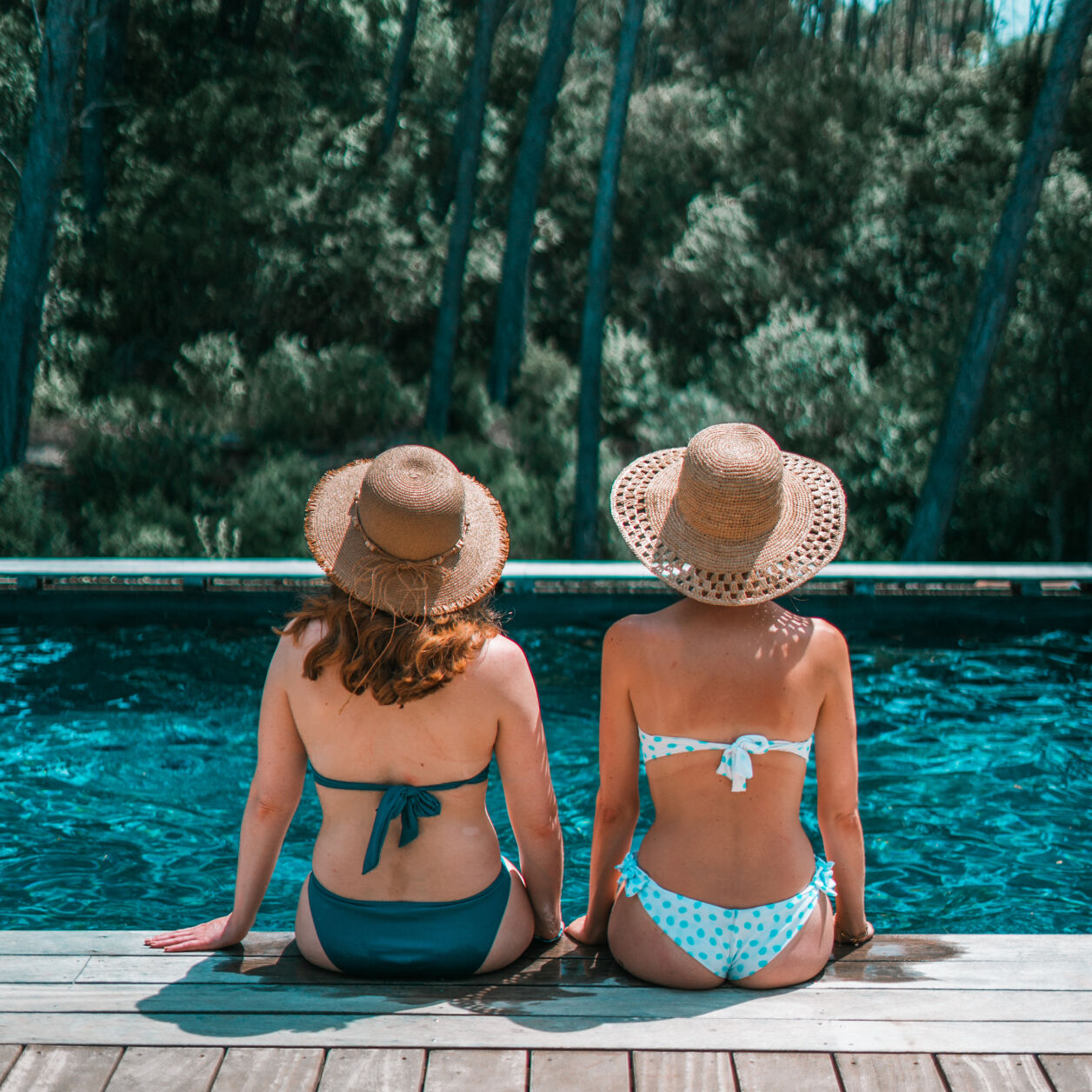 2 femmes assises sur le bord d'une piscine de dos